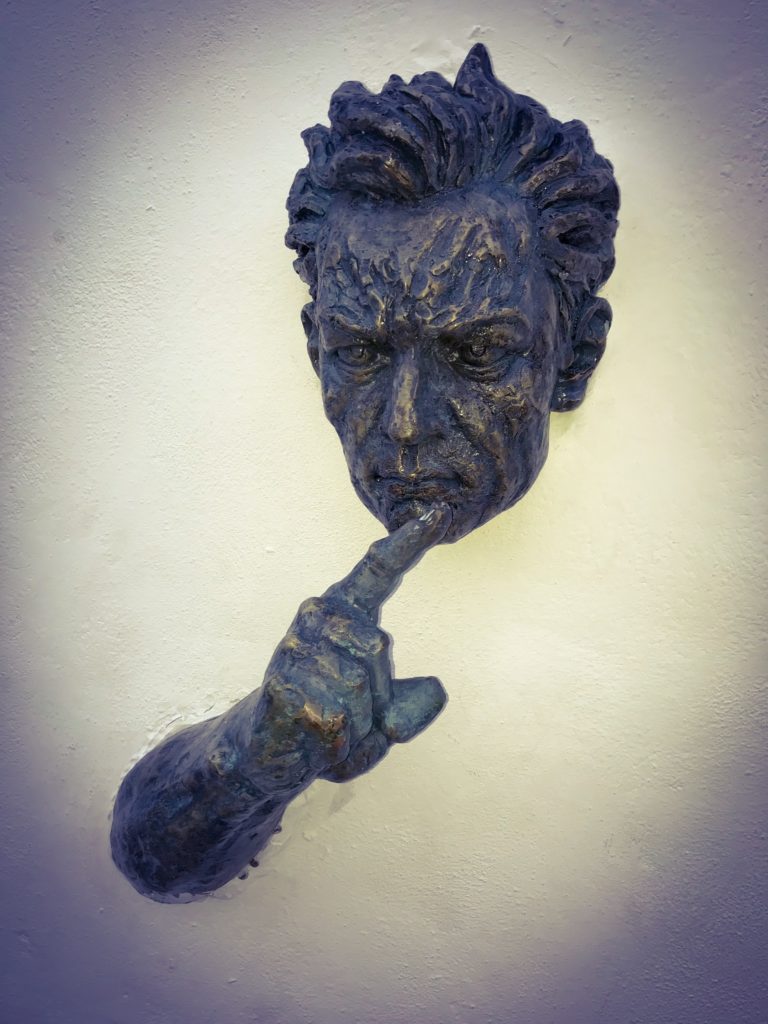 Sculpture of a man face's and hand coming out of a wall 
