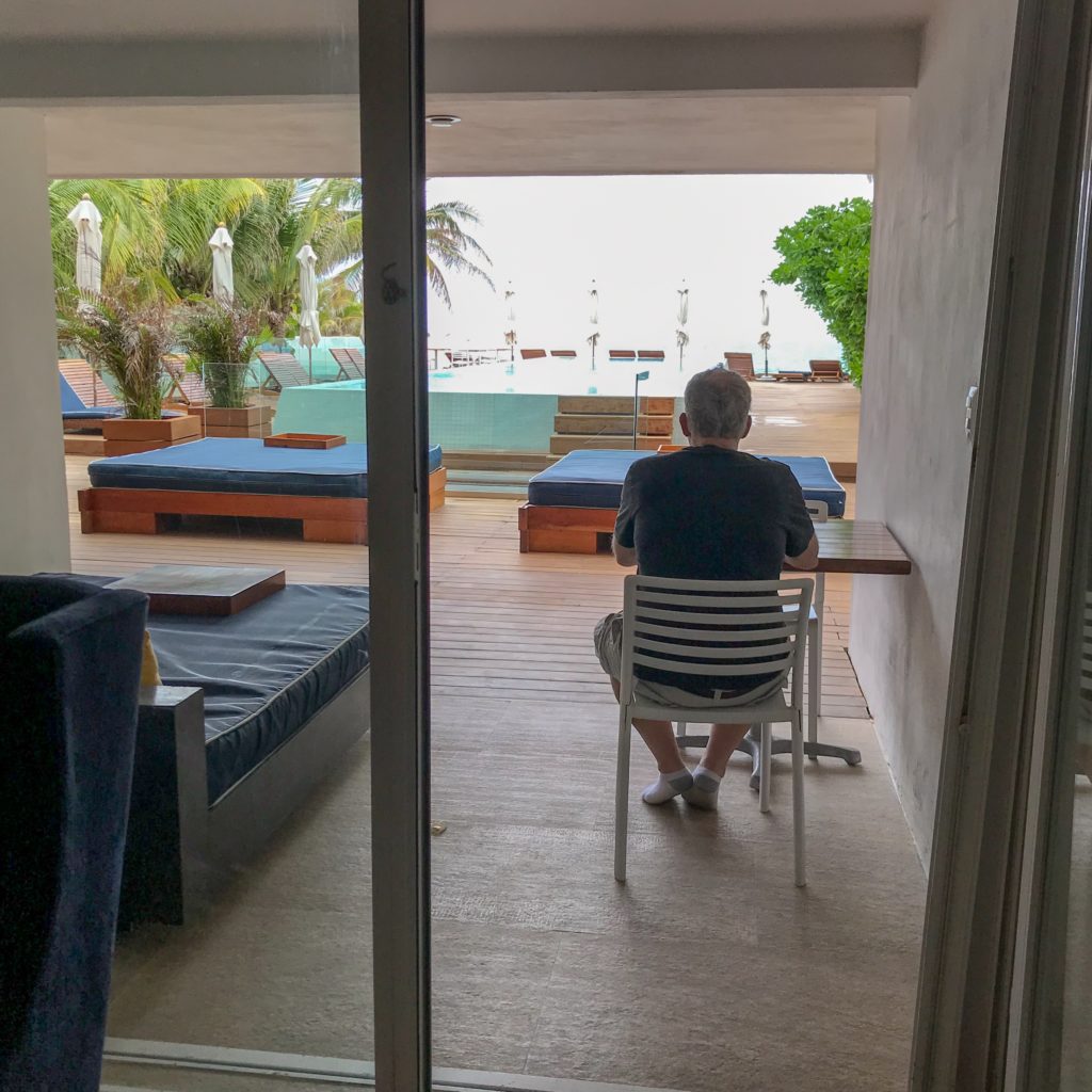 Man sitting on a hotel room terrace overlooking the pool and daybeds