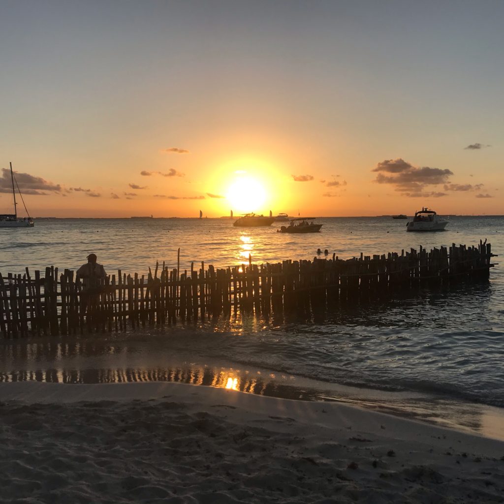 North Beach Isla Mujeres Mexico sunset with boats in the water and a fence 