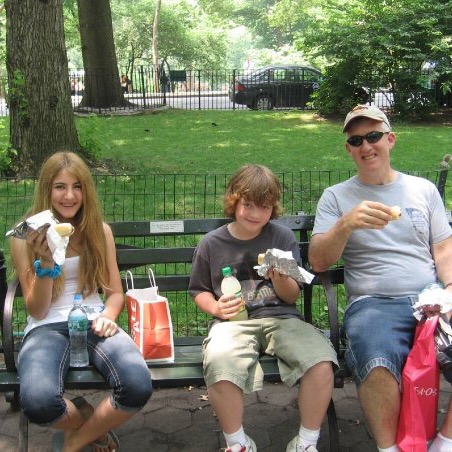 Girl, boy and man eating Nathan's famous hot dogs on a Central Park bench in New York City 