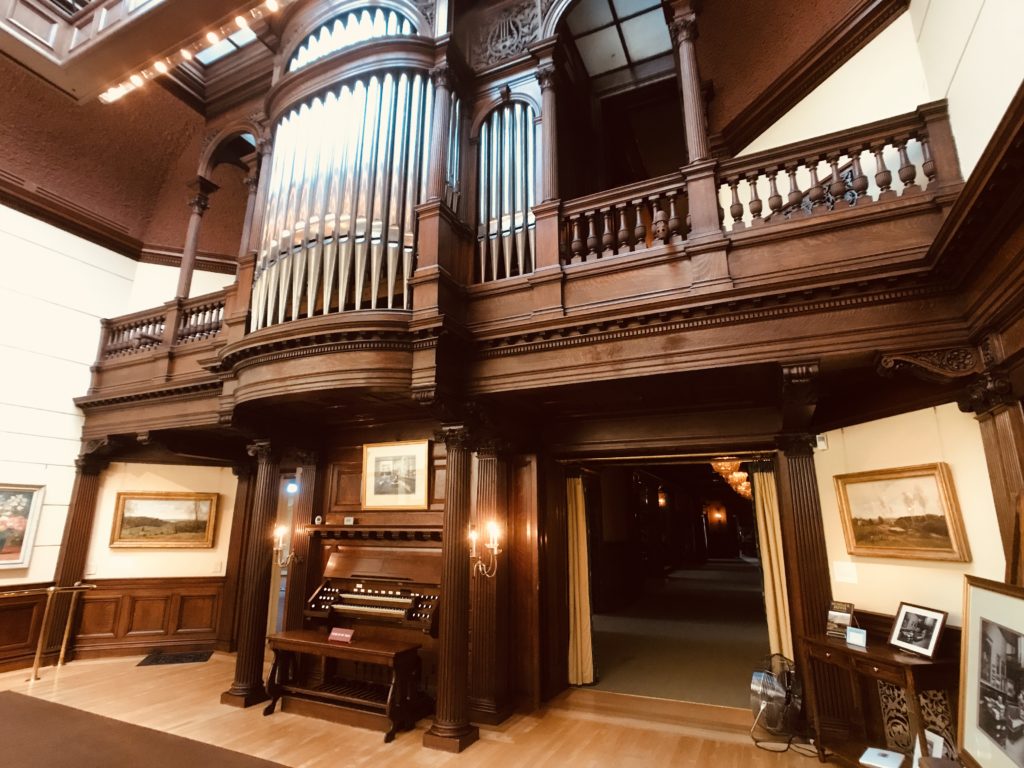 A three-story pipe organ made of mahogany wood with paintings and artwork on the walls and on display 