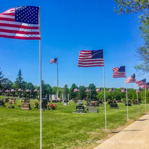 Cemetery with flags blowing in the wind, green grass, headstones and blue sky