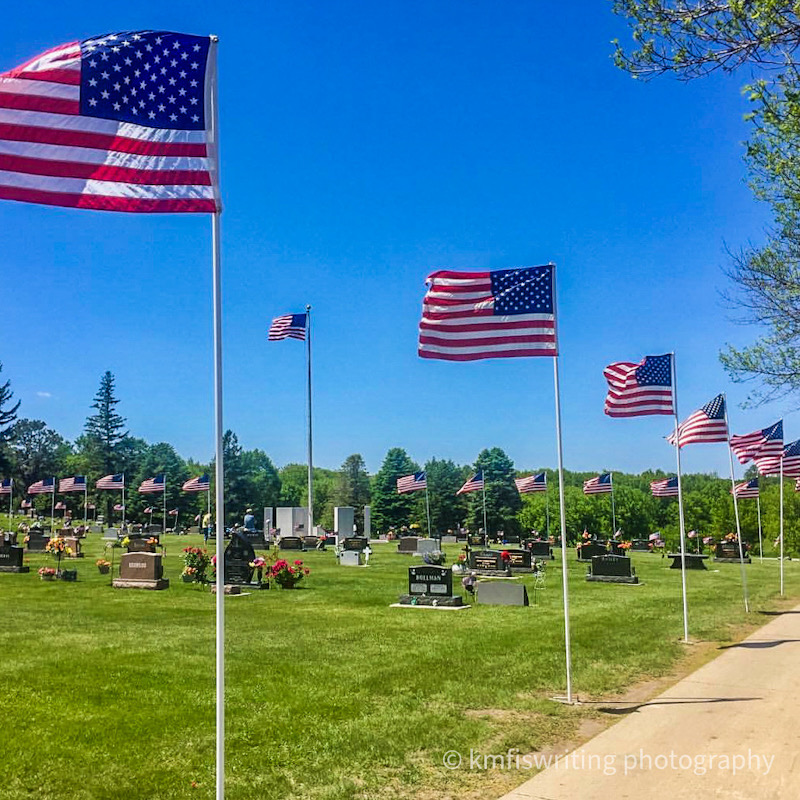 Cemetery with flags blowing in the wind, green grass, headstones and blue sky
