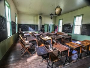 History Center of Olmsted County in Rochester, Minn. - Hadley Valley Schoolhouse a 1800s one-room schoolhouse image from the back of the classroom showing student desks, teacher's desk and blackboards and historic kerosene lamp