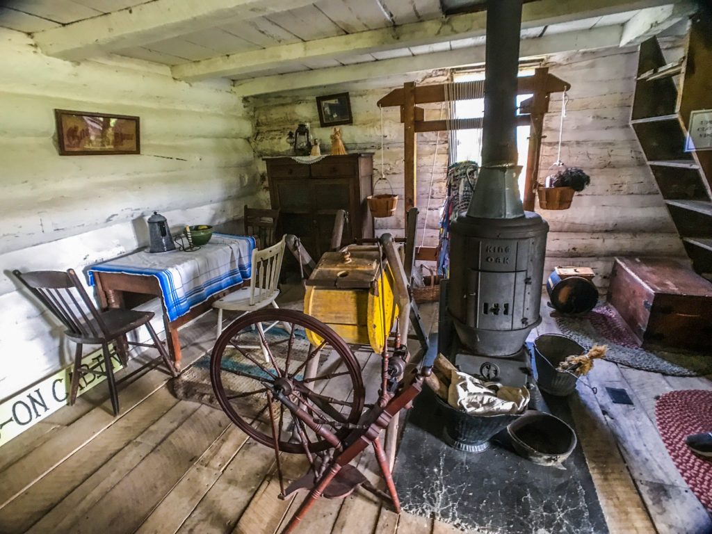 Old spinning wheel, stove and furniture inside log cabin