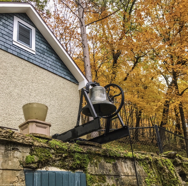 An old-fashioned dinner bell next to a vegetable cellar and fall trees - Mayowood Mansion