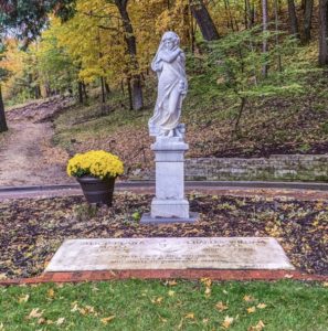 statue overlooking gravesite and headstone with fall colors in the background