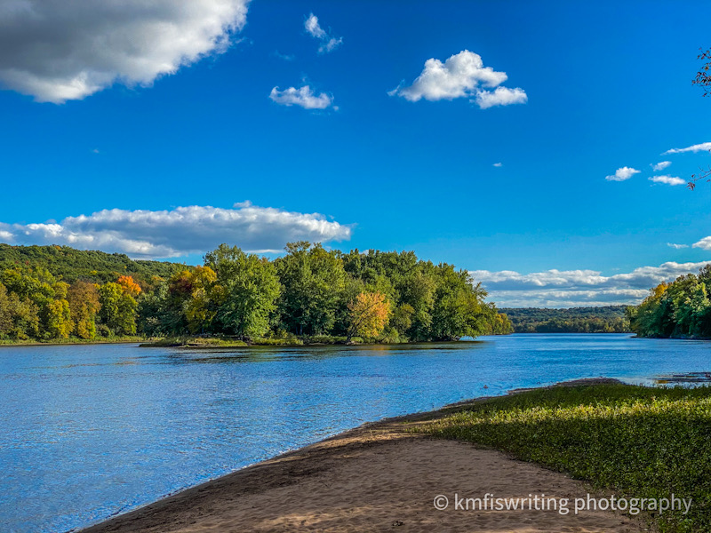 Secluded sandy beach on a river with trees just staring to turn fall colors