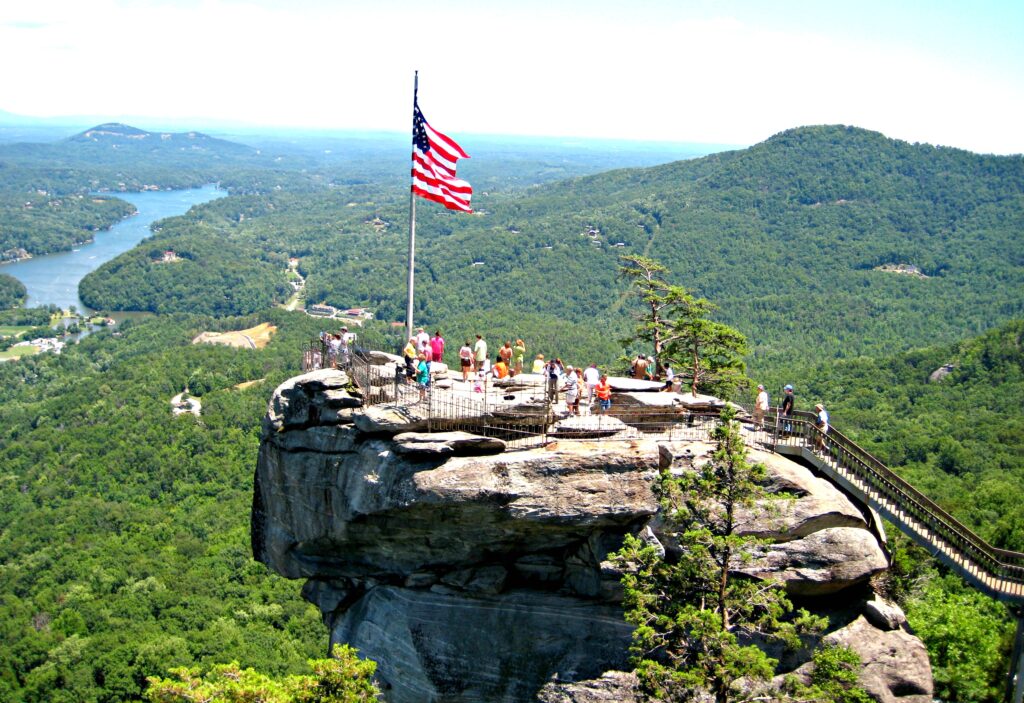 Flag and people on a rocky outcrop overlooking valleys and mountains