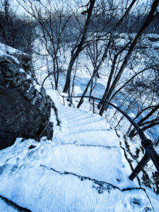 Snow-covered staircase along bluffs leading down to a frozen creek