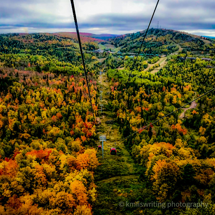 View from the top of a mountain overlooking fall foliage and a lake on a gondola ride