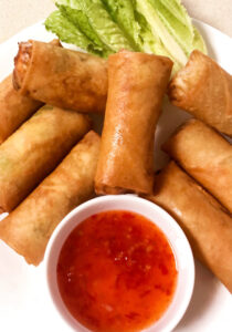 Egg rolls with dipping chili sauce in a bowl with lettuce garnish