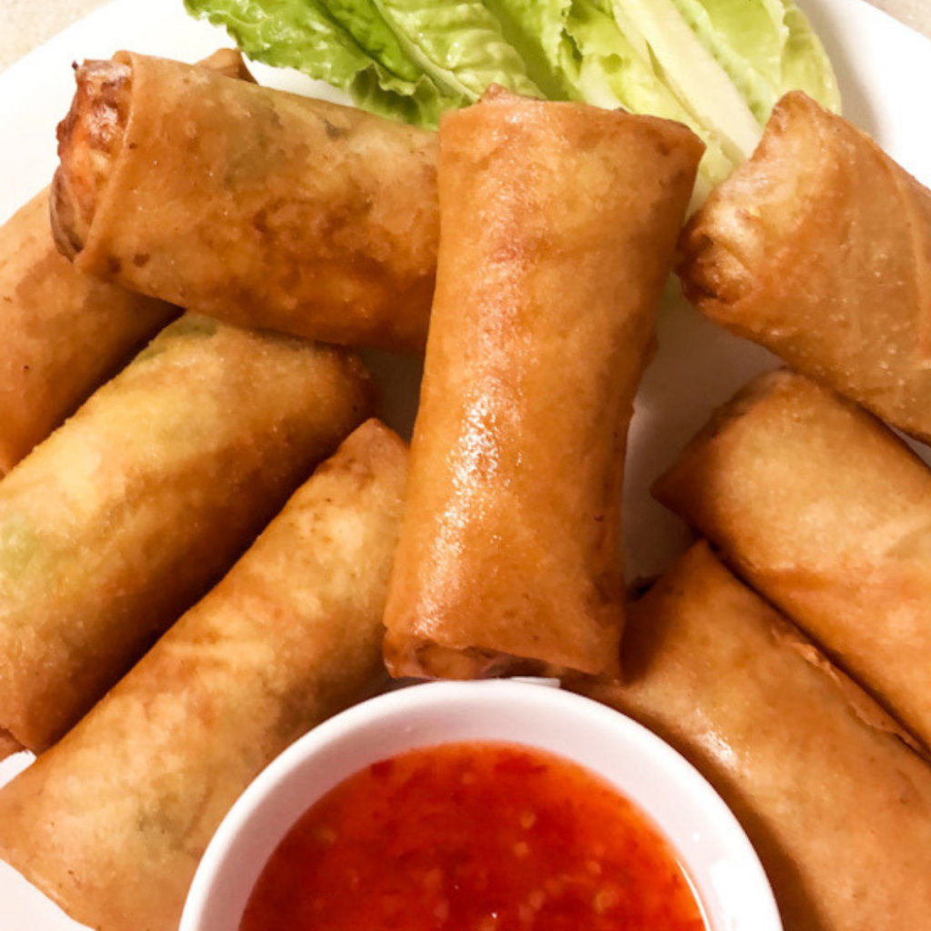 Egg rolls on a platter with a dish of dipping sauce and green lettuce garnish