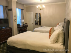 two beds with white comforters in hotel room with desk and chandelier