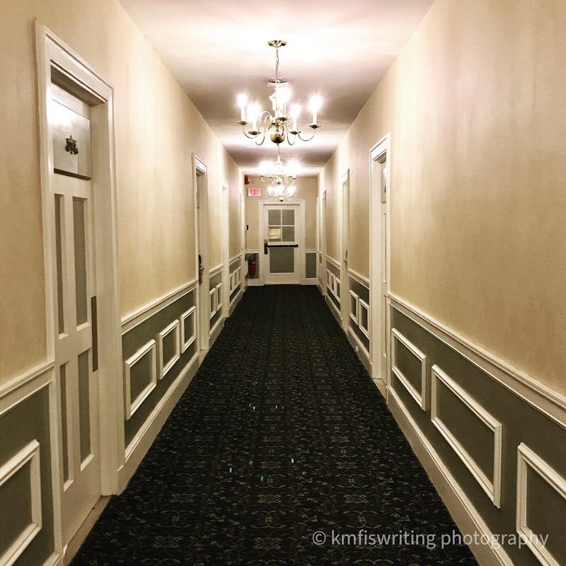 Carpeted hallway with doors and paneled walls and chandelier