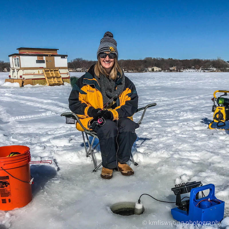 Woman ice fishing on a frozen lake in Minnesota with ice fishing house in background