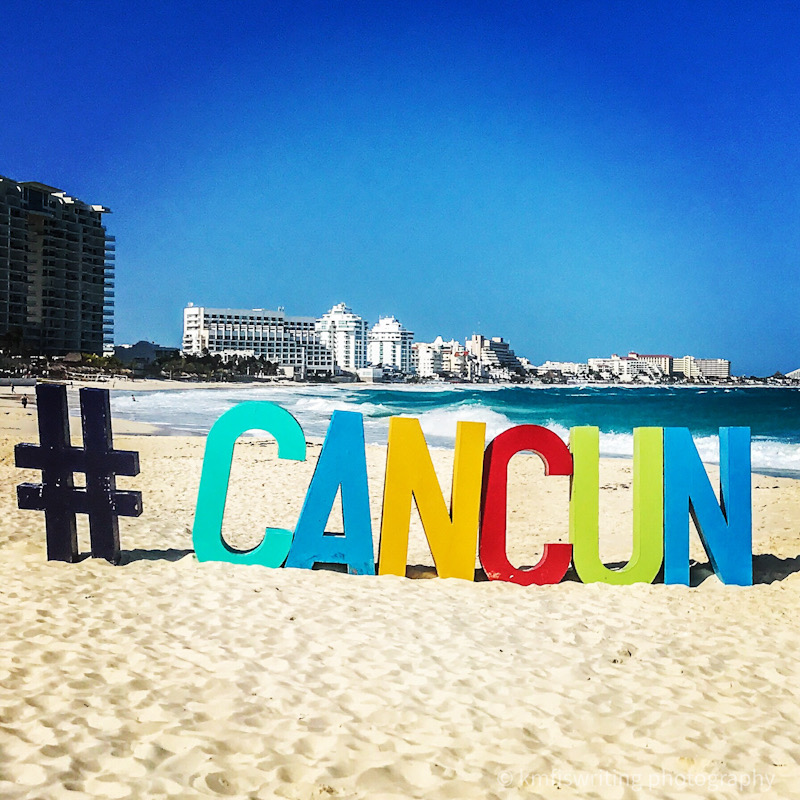 Cancun sign in colorful letters on the beach with the skyline behind
