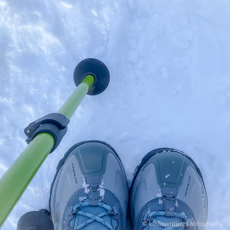 Trekking walking pole on snow and a pair of snow boots