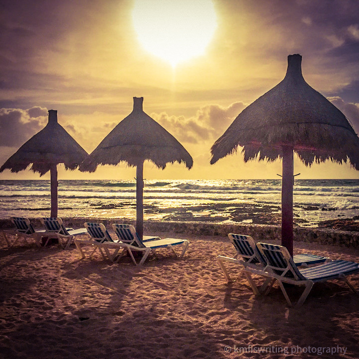 Sunrise with beach chairs, thatched umbrellas next to ocean
