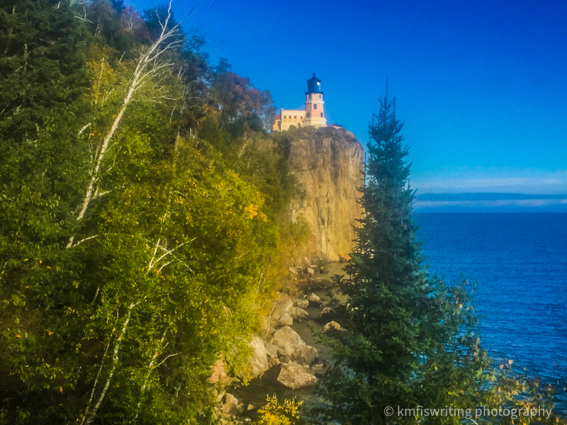 Lighthouse on a cliff overlooking a lake with trees in the foreground
