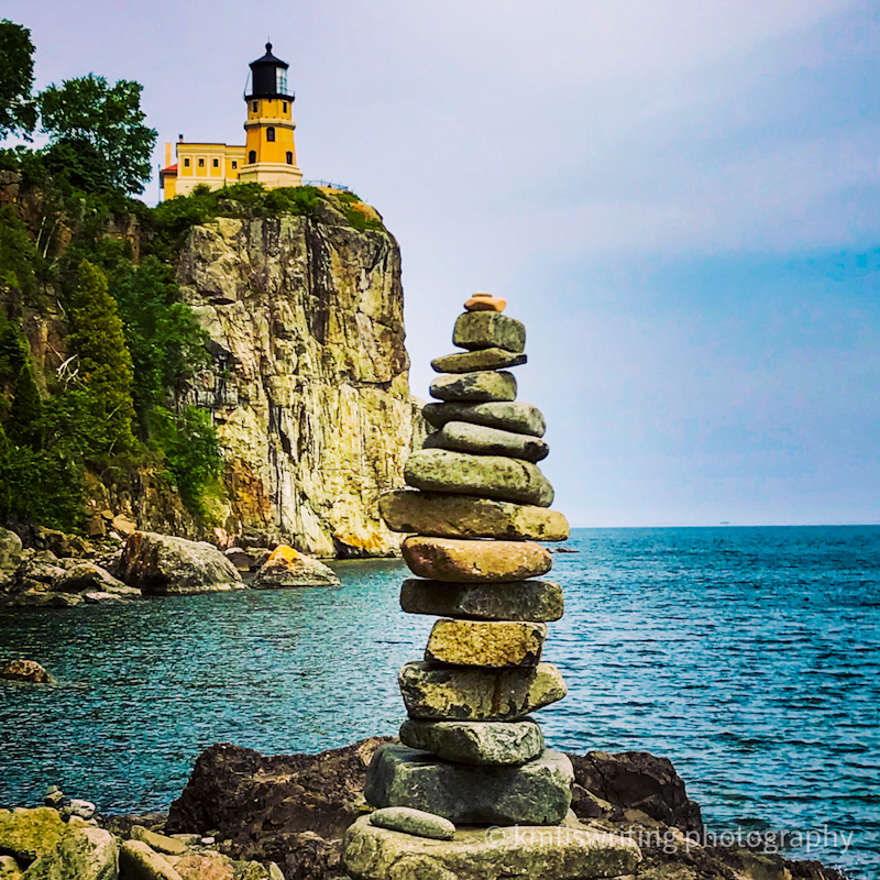 Lighthouse on a cliff with rocks stacked up on the shore